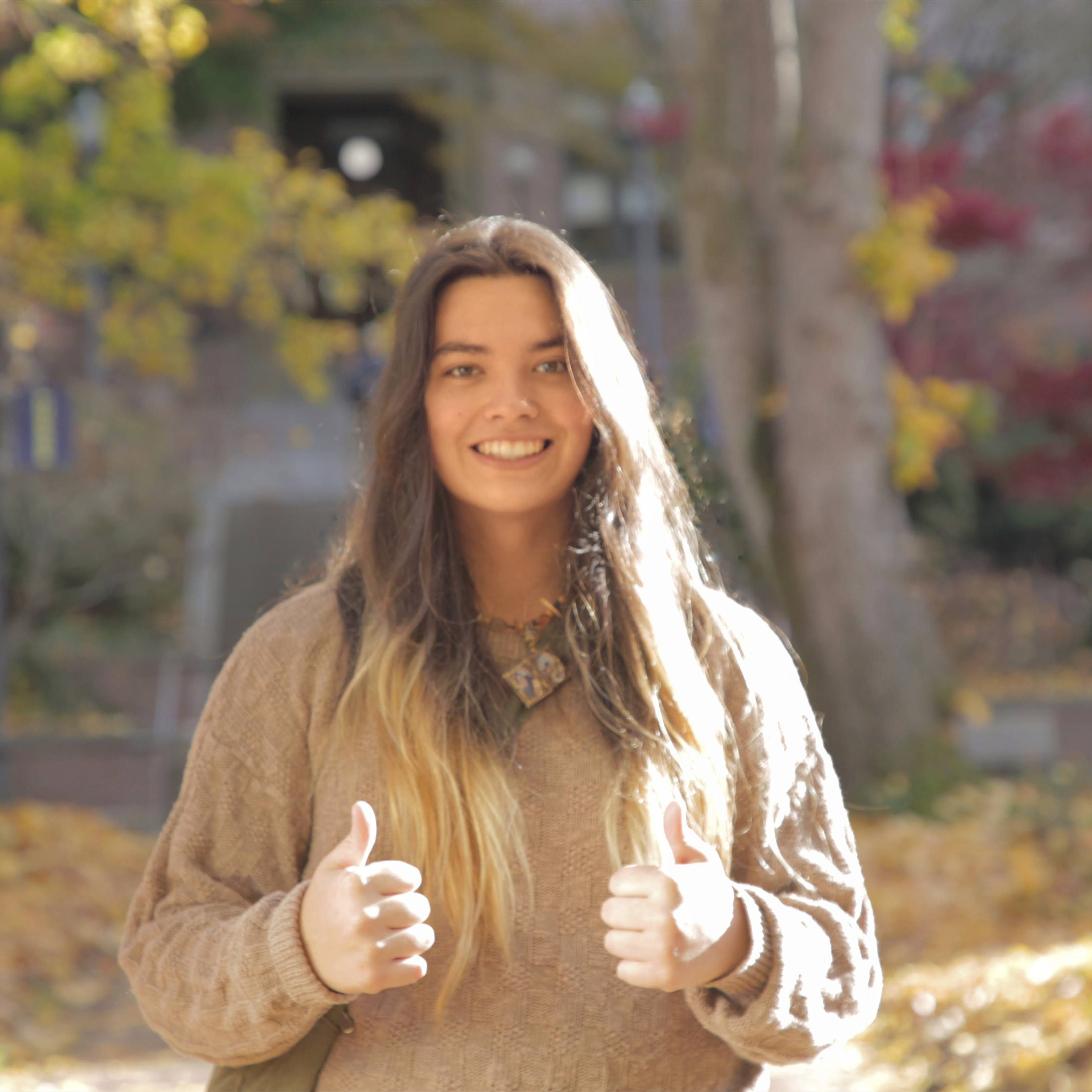 Lola Thompson gives a "two thumbs-up," standing in front of Old Main